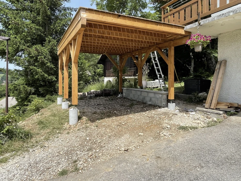 Chantier extérieur de construction d'un carport en bois avec structure à poteaux et charpente traditionnelle