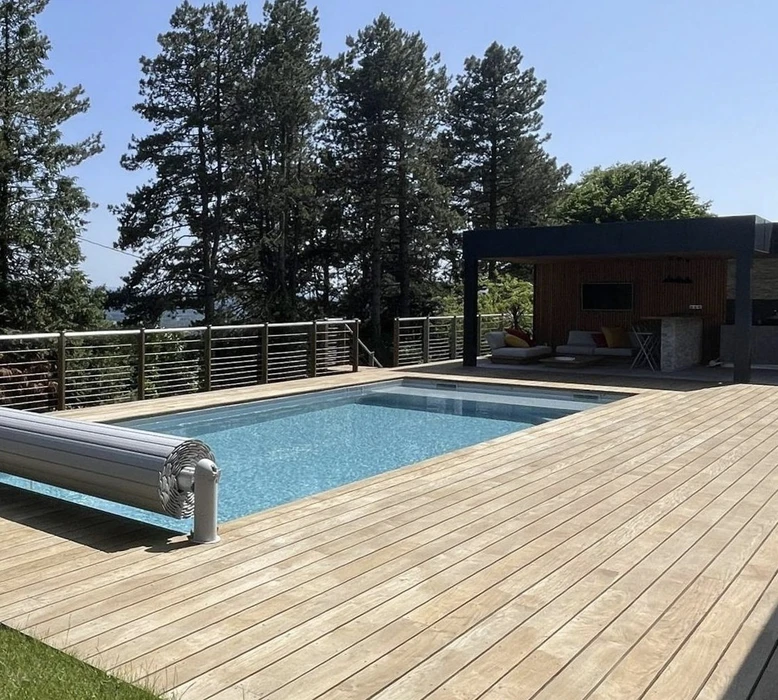 Terrasse extérieure avec piscine rectangulaire à débordement, entourée de platelage bois