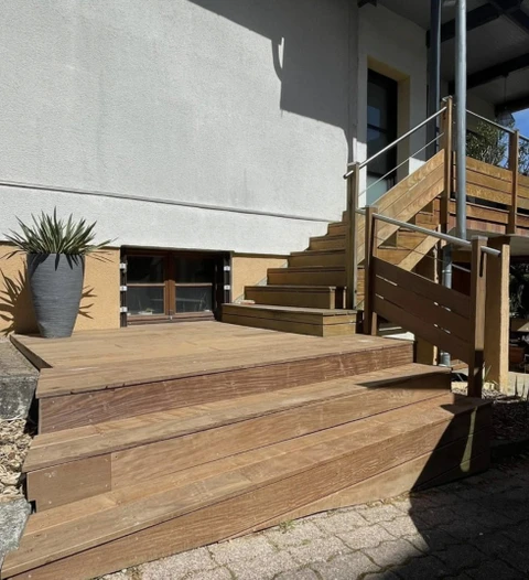 Escalier extérieur en bois avec terrasse et garde-corps métalliques, menant à l'étage d'une maison moderne