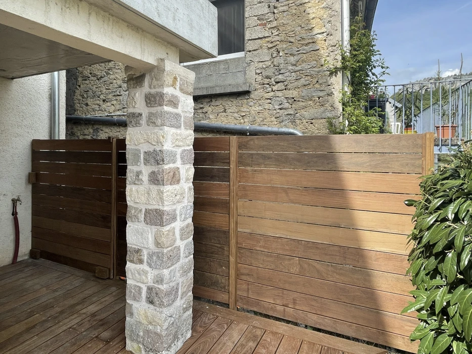Extérieur résidentiel avec clôture en bois exotique à lames horizontales, pilier en pierre naturelle calcaire, mur en moellons traditionnels