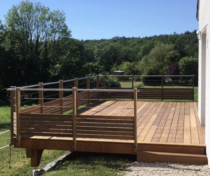 Terrasse extérieure surélevée en bois avec garde-corps horizontal et câbles métalliques, située devant maison moderne